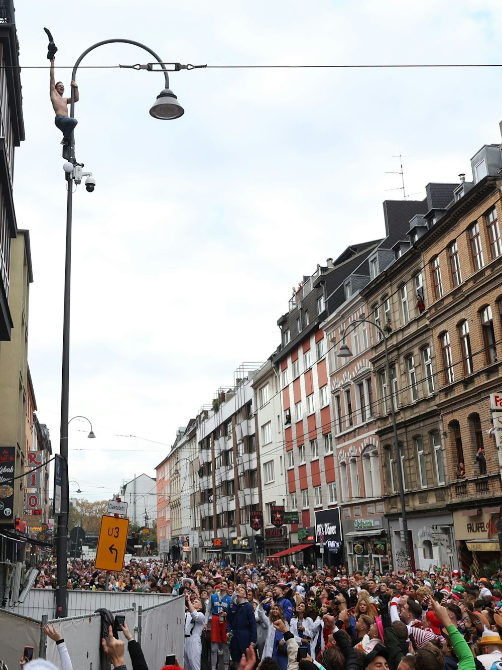 Ein Mann steht auf einer Überwachungskamera, die oben an einer Straßenlaterne befestigt ist und jubelt.