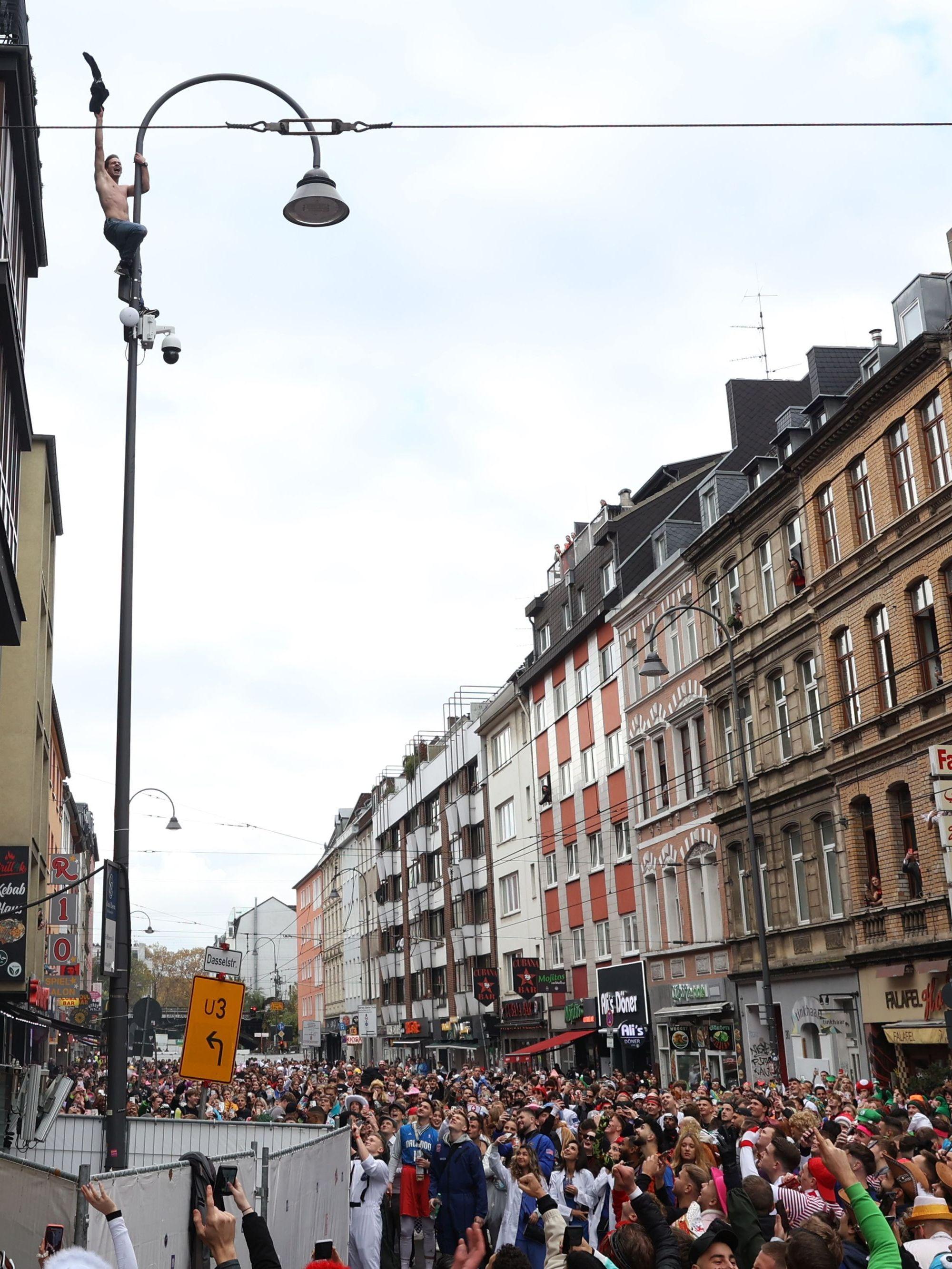 Ein Mann steht auf einer Überwachungskamera, die oben an einer Straßenlaterne befestigt ist und jubelt.