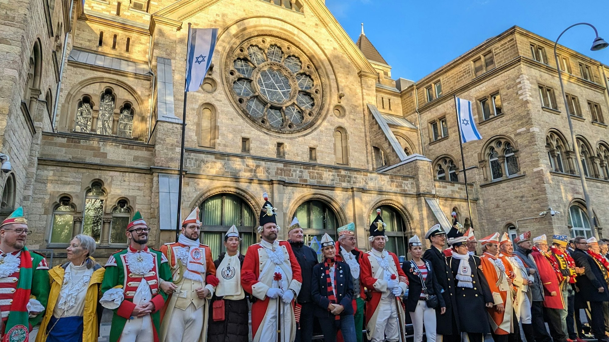 Karnevalisten stellen sich vor der Synagoge in einer Menschenkette auf, um gegen Antisemitismus zu protestieren.