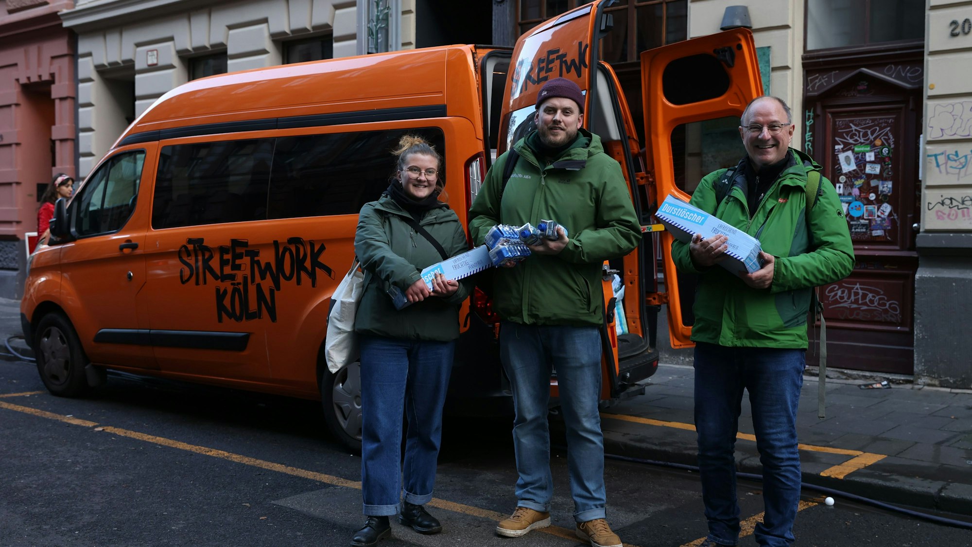 Streetworker Lisa Gindler, Lasse Golob und Uwe Schärpf stehen vor ihrem Kleinbus, haben Snacks und Getränke in der Hand und bereiten sich auf ihren Rundgang vor.