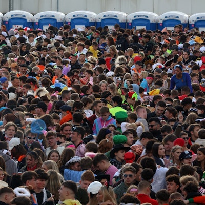 Jecke drängeln sich vor Dixie-Klos auf einer umzäunten Fläche.