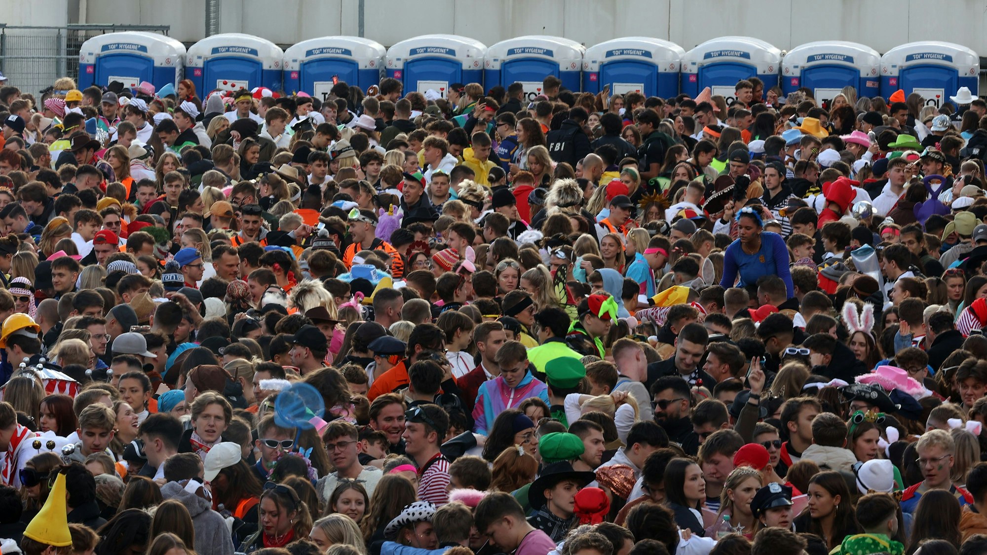 Jecke drängeln sich vor Dixie-Klos auf einer umzäunten Fläche.