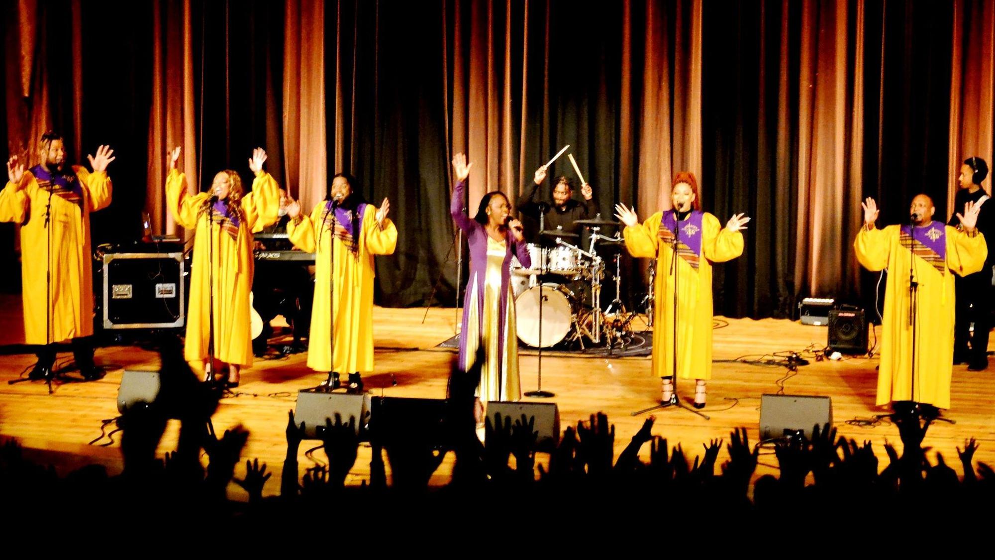 Die Gospelsängerinnen performen in gelben Gewändern auf der Bühnen, während die Zuschauer im Vordergrund die Hände hochrecken.