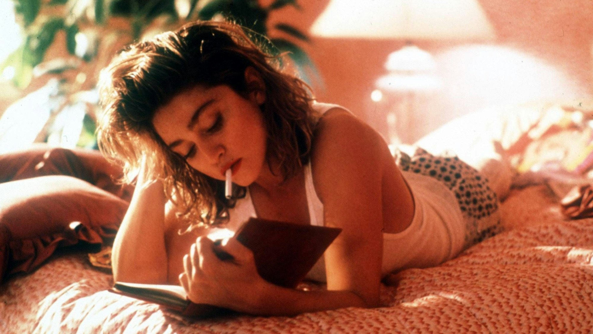 Madonna als Susan, rauchend im Bett, während sie ein Buch liest.