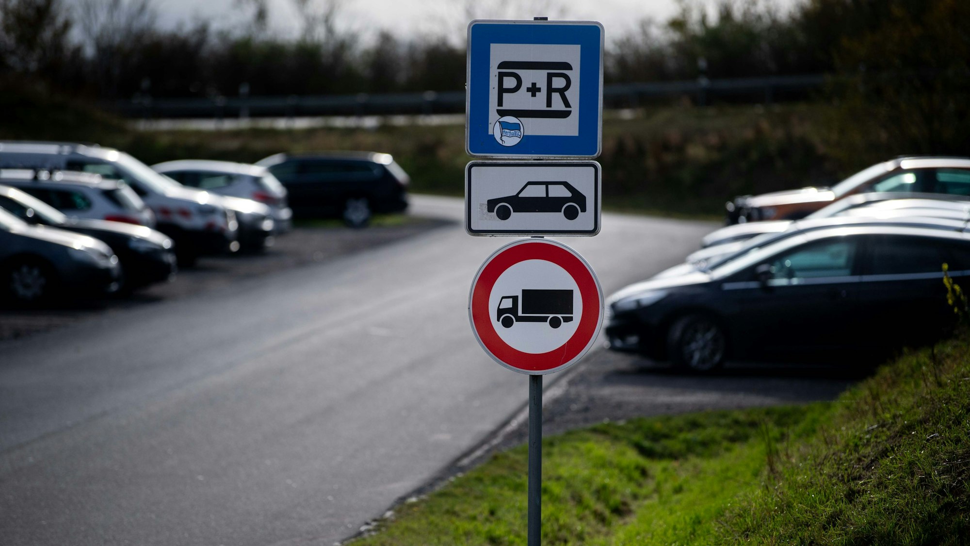 Das Bild zeigt den Pendlerparkplatz in Weilerswist. Zu sehen sind mehrere Schilder und im Hintergrund geparkte Autos.