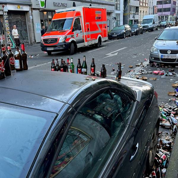 Bierflaschen stehen auf dem Dach eines geparkten Autos, auch auf der Straße liegen Berge von Glasflaschen.
