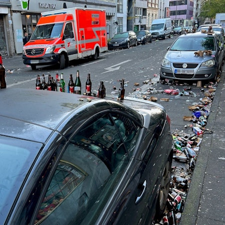 Bierflaschen stehen auf dem Dach eines geparkten Autos, auch auf der Straße liegen Berge von Glasflaschen.
