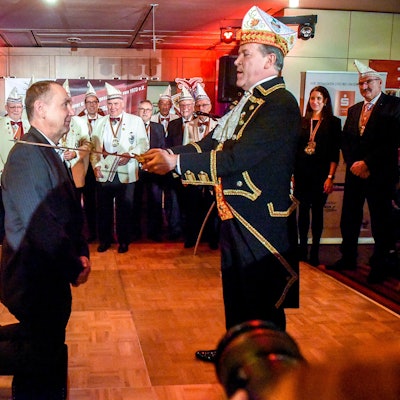 Ein Mann kniet, ein anderer berührt ihn mit einem Schert an der Schulter.