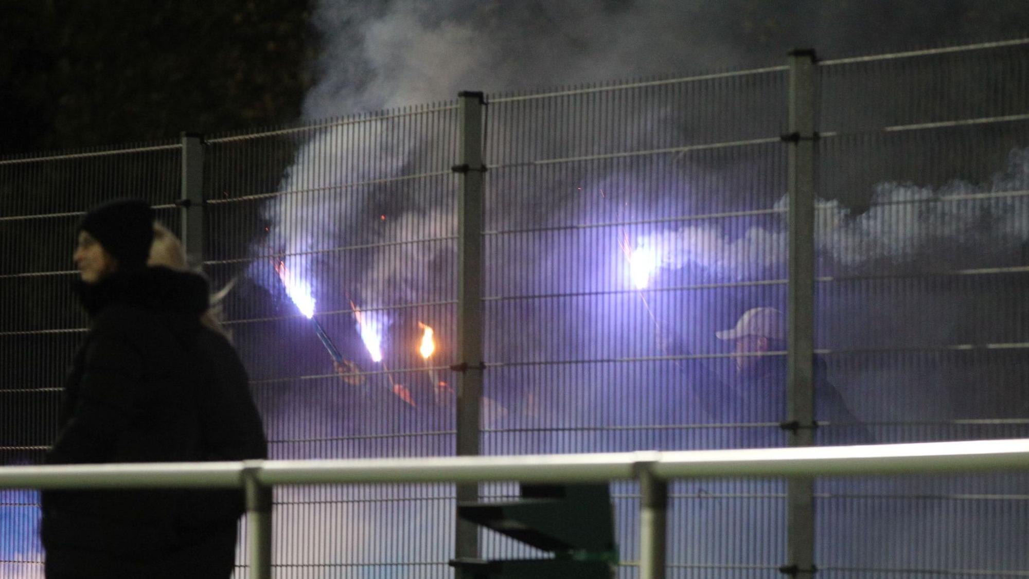 Fans der Sportfreunde D-H-O stehen hinter dem Zaun und zündeten Bengalos an.