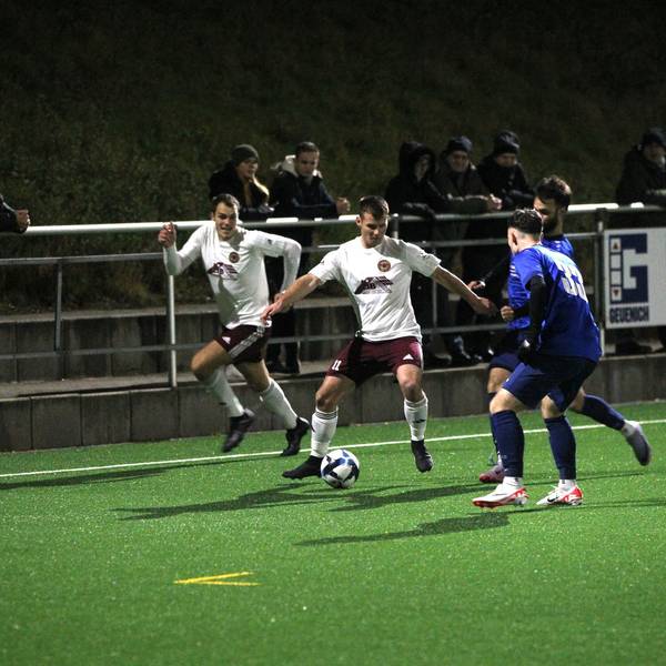 Lommersums Marcel Ebel hat den Ball und wird von zwei Gegenspielern bedrängt. Ein Mitspieler hinterläuft Ebel.