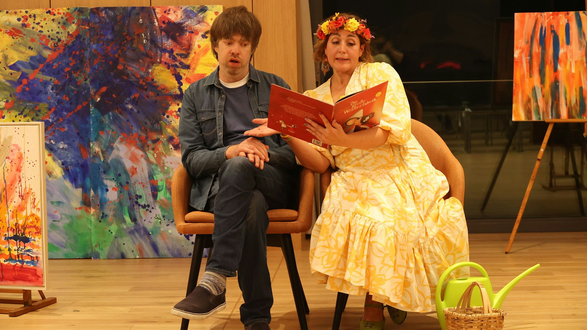 Erik Körmann und Ana Bela Gomez sitzen auf der Bühne auf Stühlen, sie liest ihm etwas vor.