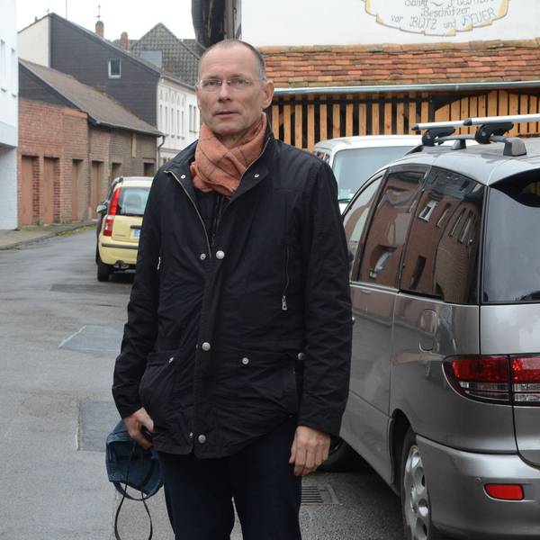 Ein Mann steht auf einer engen Straße. Die Gehwege sind sehr schmal, links und rechts parken Autos.