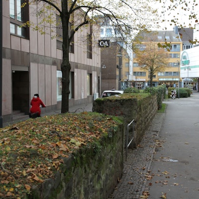 Blätter und Moos auf einer alten Stadtmauer zwischen einer C&A und einer Kaufhof-Filiale
