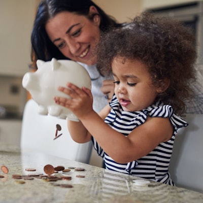 Ein kleines Mädchen leert zusammen mit der Mutter sein Sparschwein aus.