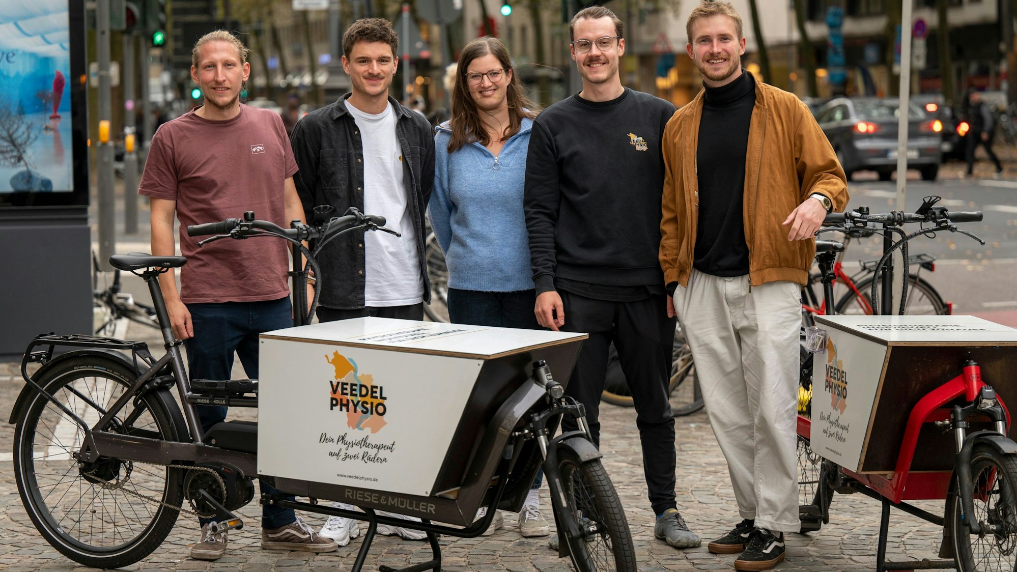 Zu sehen sind fünf Menschen vor zwei Elektro-Lastenrädern in Köln.