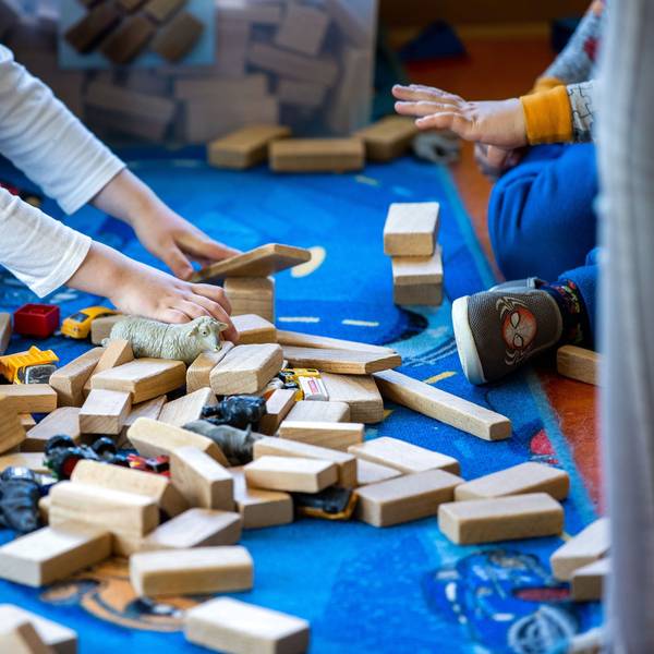 Bauklötze und anderes Spielzeug liegen auf dem Boden. Man sieht die Hände und die Füße von zwei Kindern.