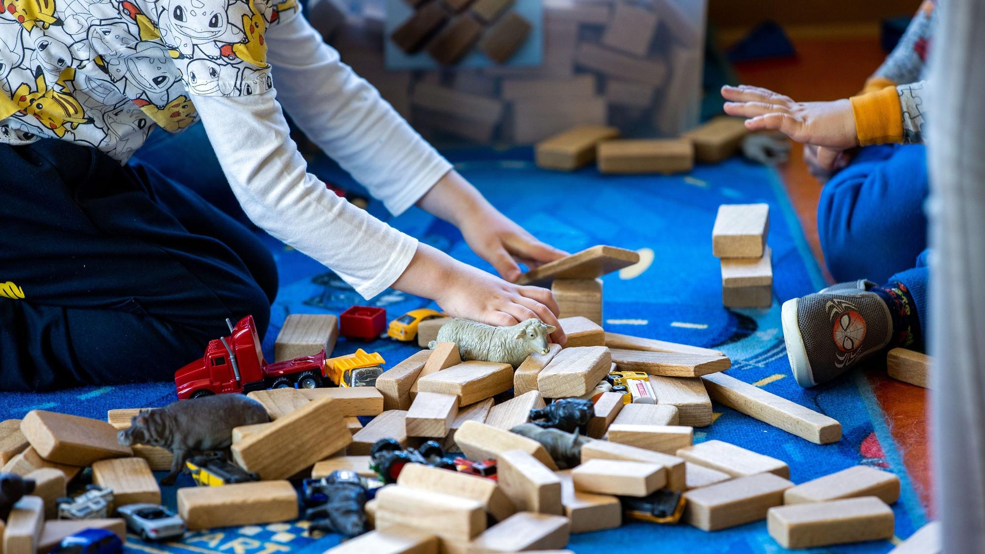 Bauklötze und anderes Spielzeug liegen auf dem Boden. Man sieht die Hände und die Füße von zwei Kindern.