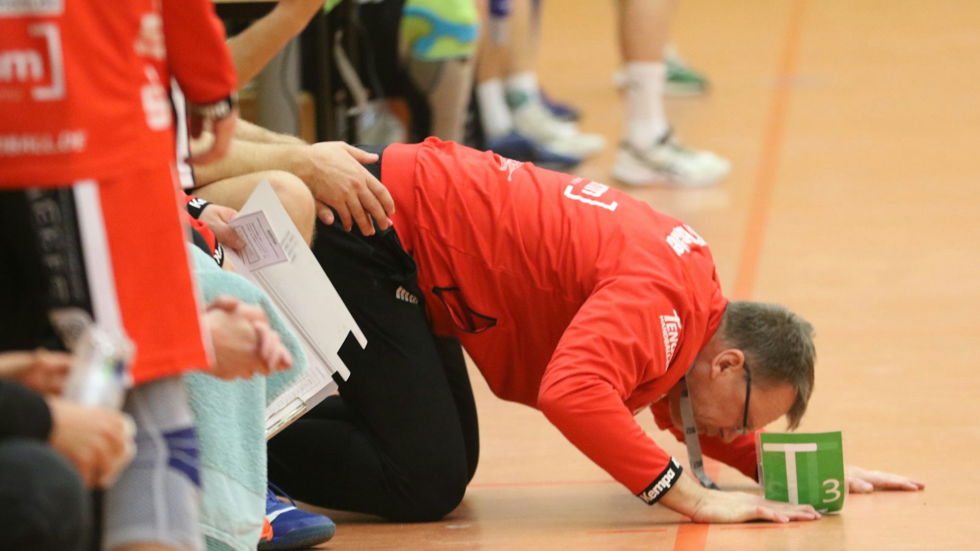 HSG-Euskirchen-Trainer Marco Matheis kniet auf dem Boden, den Kopf fast auf dem Parkett liegend.