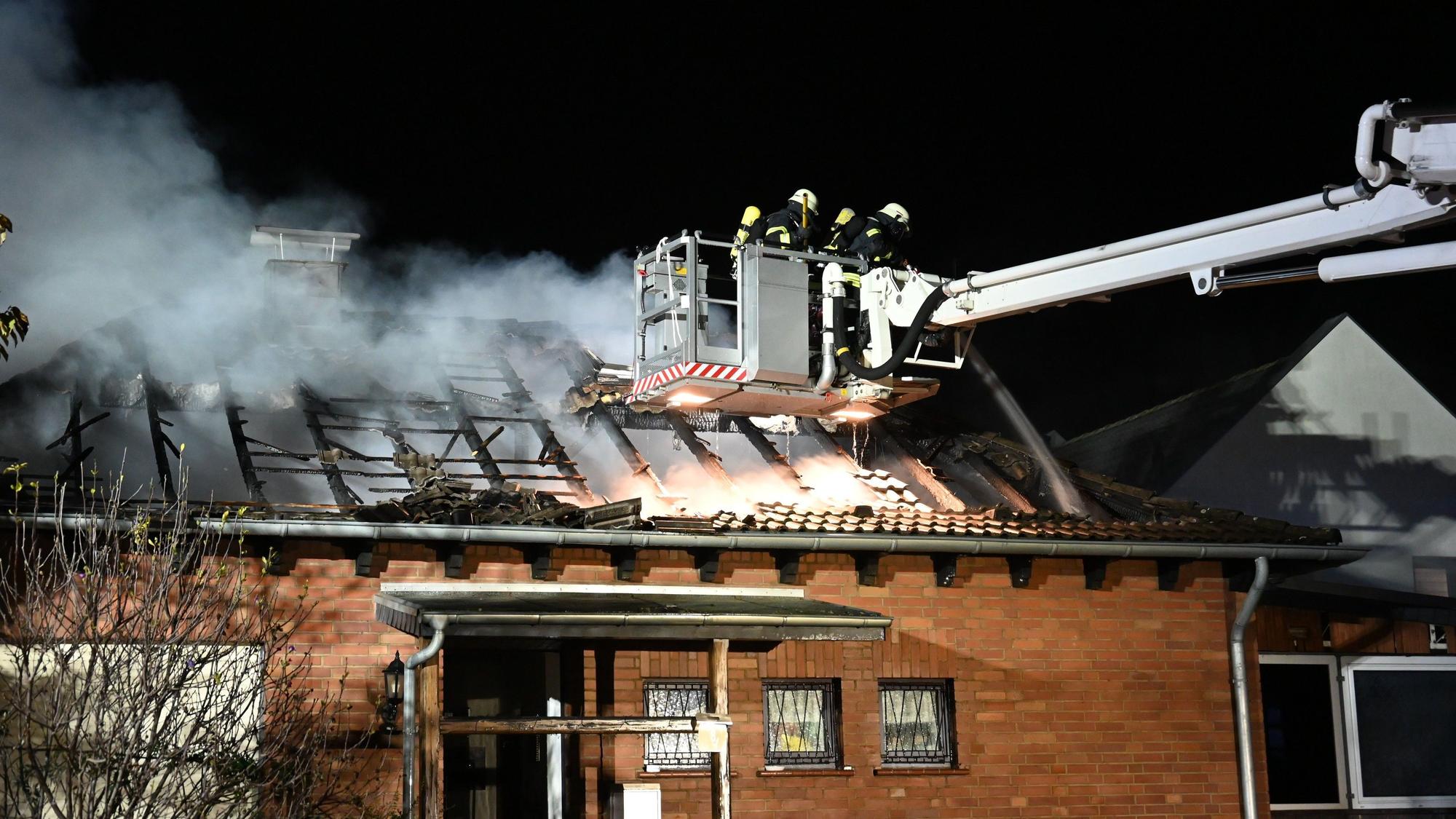 Feuerwehrleute auf einer Drehleiter löschen den Brand in einem Bungalow in Kerpen-Sindorf.
