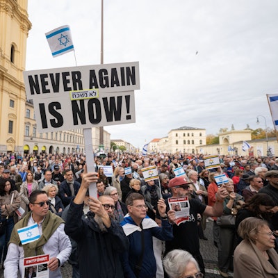 Ein Teilnehmer der Kundgebung "Solidarität mit Israel - Gegen gegen Terror, Hass und Antisemitismus" hält ein Schild mit der Aufschrift "NEVER AGAIN IS NOW!" in die Höhe.