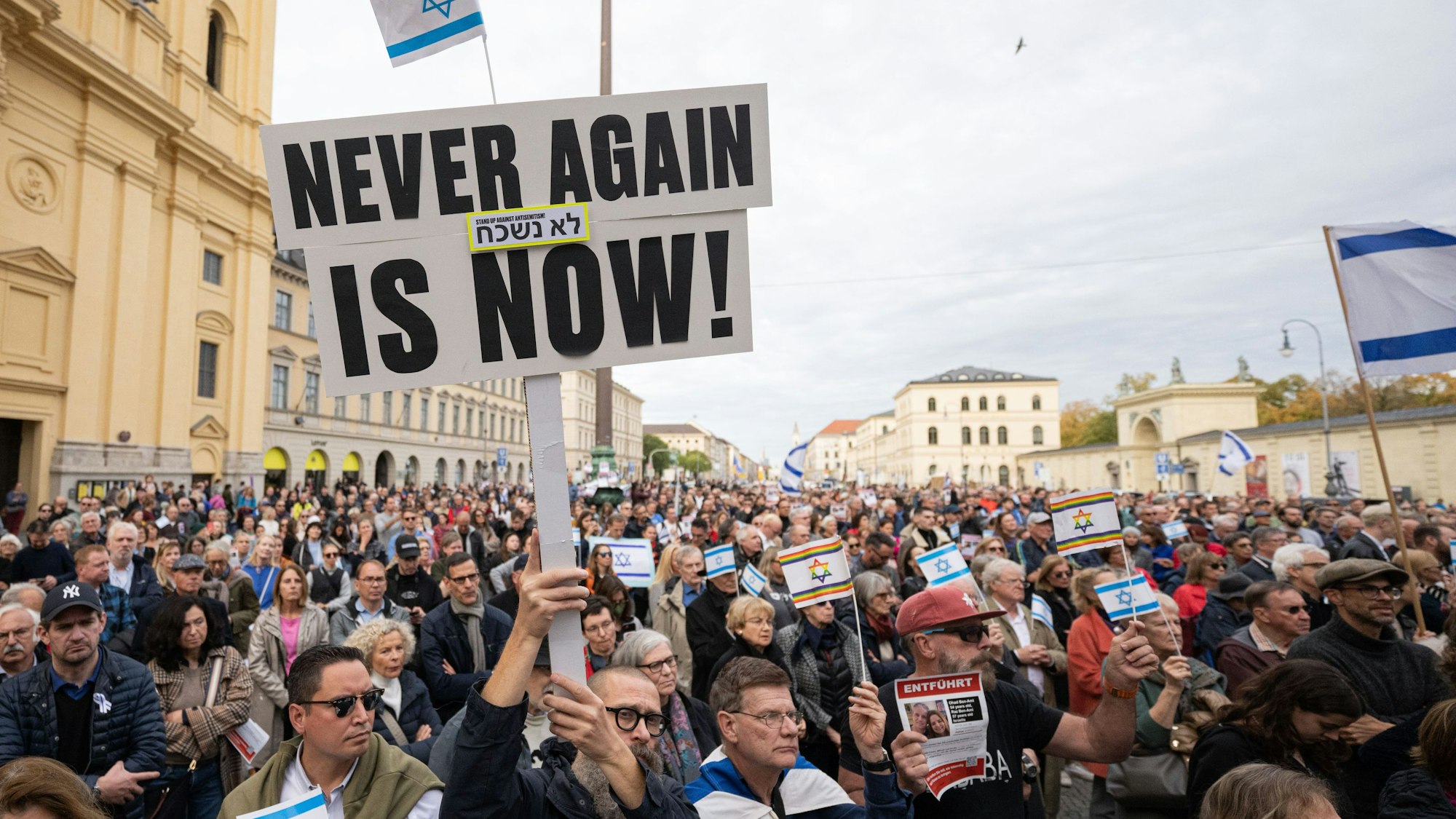 Ein Teilnehmer der Kundgebung "Solidarität mit Israel - Gegen gegen Terror, Hass und Antisemitismus" hält ein Schild mit der Aufschrift "NEVER AGAIN IS NOW!" in die Höhe.