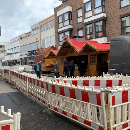 In der Berliner Straße in Euskirchen, die erneuert wird, stehen Bauzäune. Dahinter stellen mehrere Männer Verkaufsbuden für die Veranstaltung Winterzauber auf.