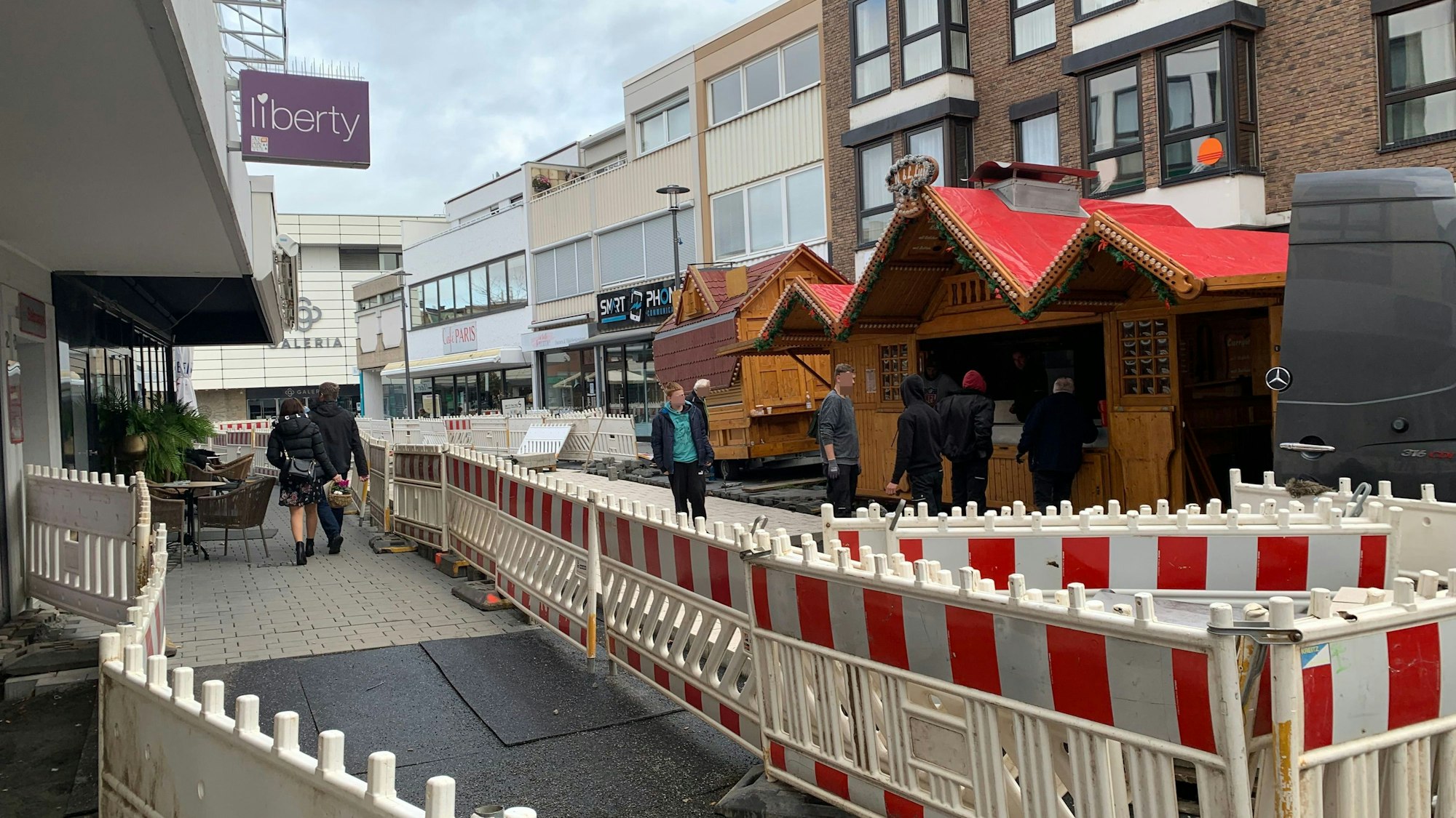 In der Berliner Straße in Euskirchen, die erneuert wird, stehen Bauzäune. Dahinter stellen mehrere Männer Verkaufsbuden für die Veranstaltung Winterzauber auf.