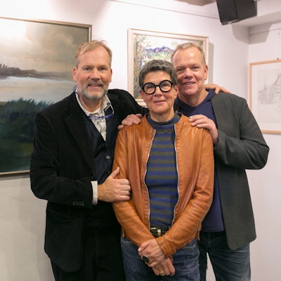Zwei Herren und eine Dame stehen vor Bildern in einem Ausstellungsraum.