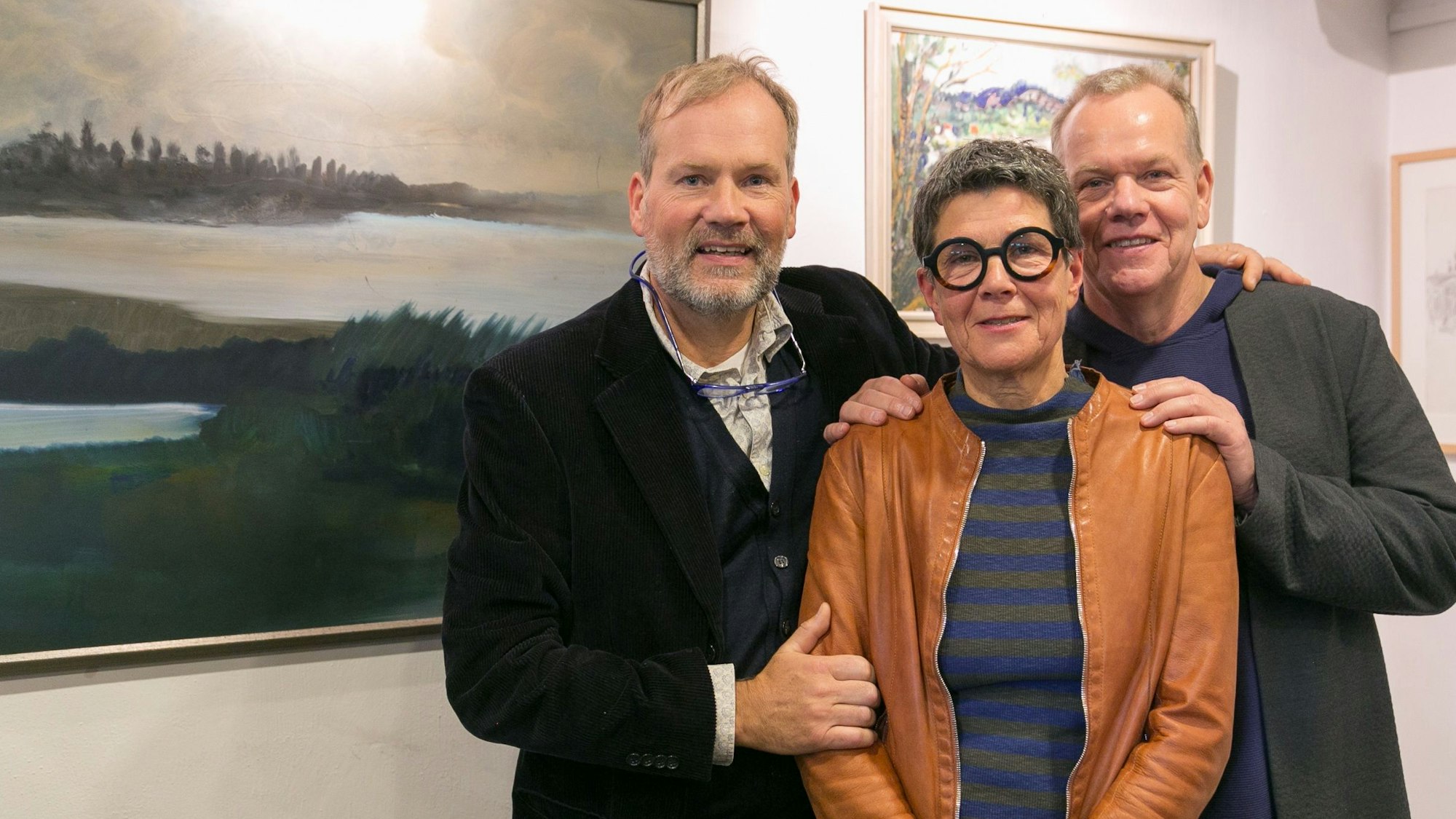 Zwei Herren und eine Dame stehen vor Bildern in einem Ausstellungsraum.