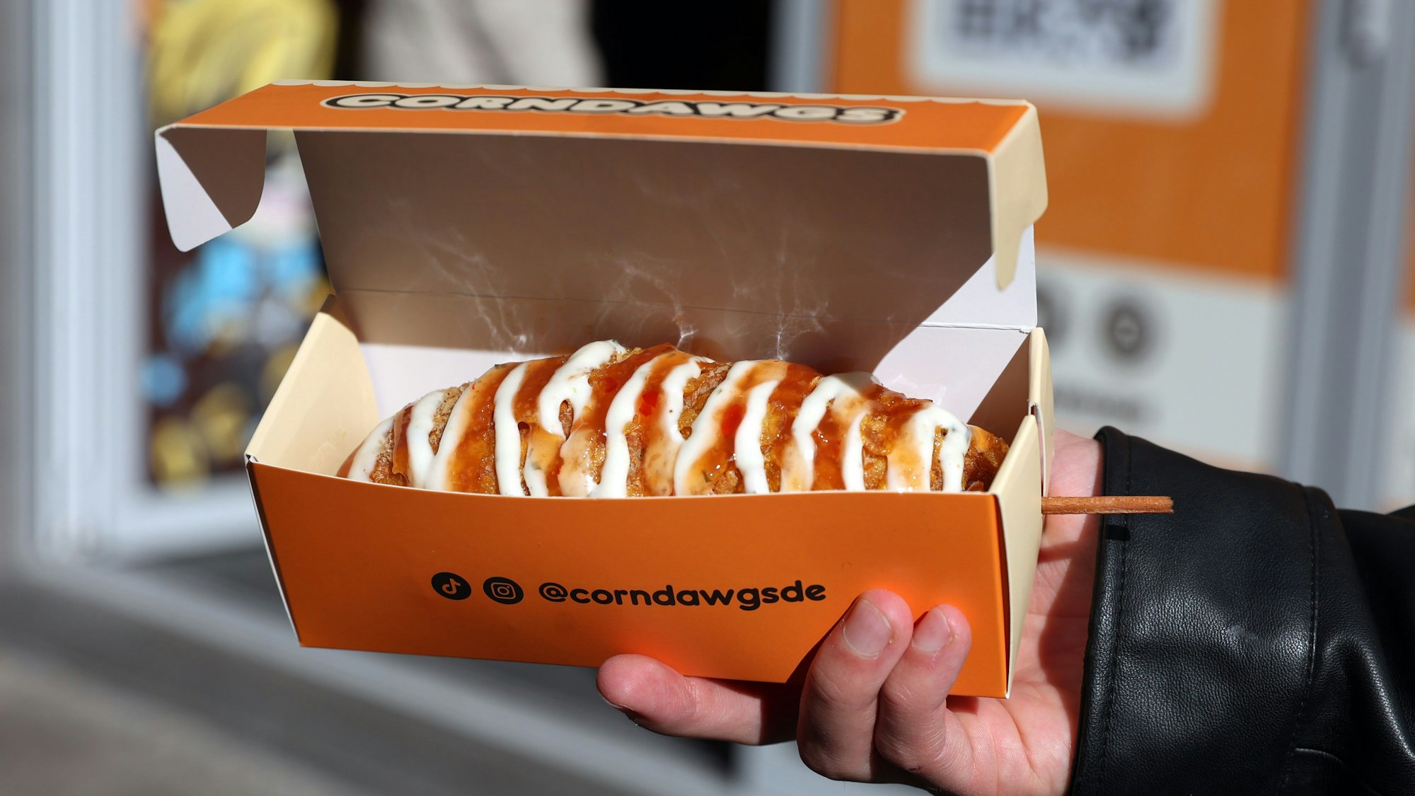 Corndogs mit Topping in orangener Verpackung.