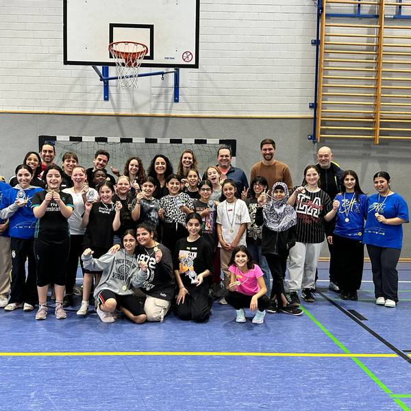 In einer Turnhalle posieren Schülerinnen mit Lehrer mit einer jungen Frau.
