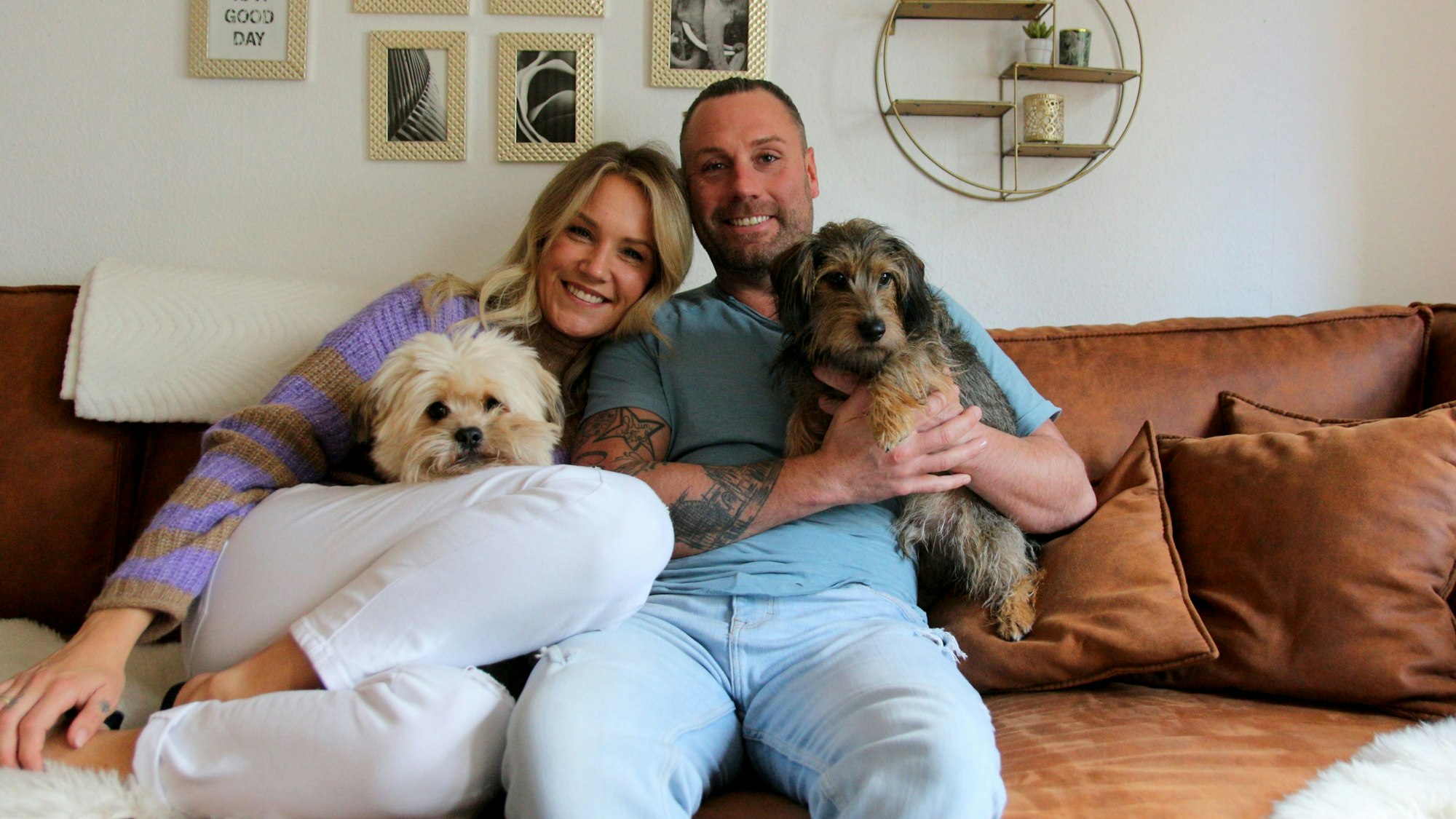 Eine Frau und ein Mann sitzen mit zwei Hunden auf einem Sofa.