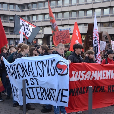 Demonstranten vor der Stadthalle, im Hintergrund ist das Troisdorfer Rathaus zu sehen. Die Demonstranten tragen Transparente mit Aufschriften wie „Nationalismus ist keine Alternative“.