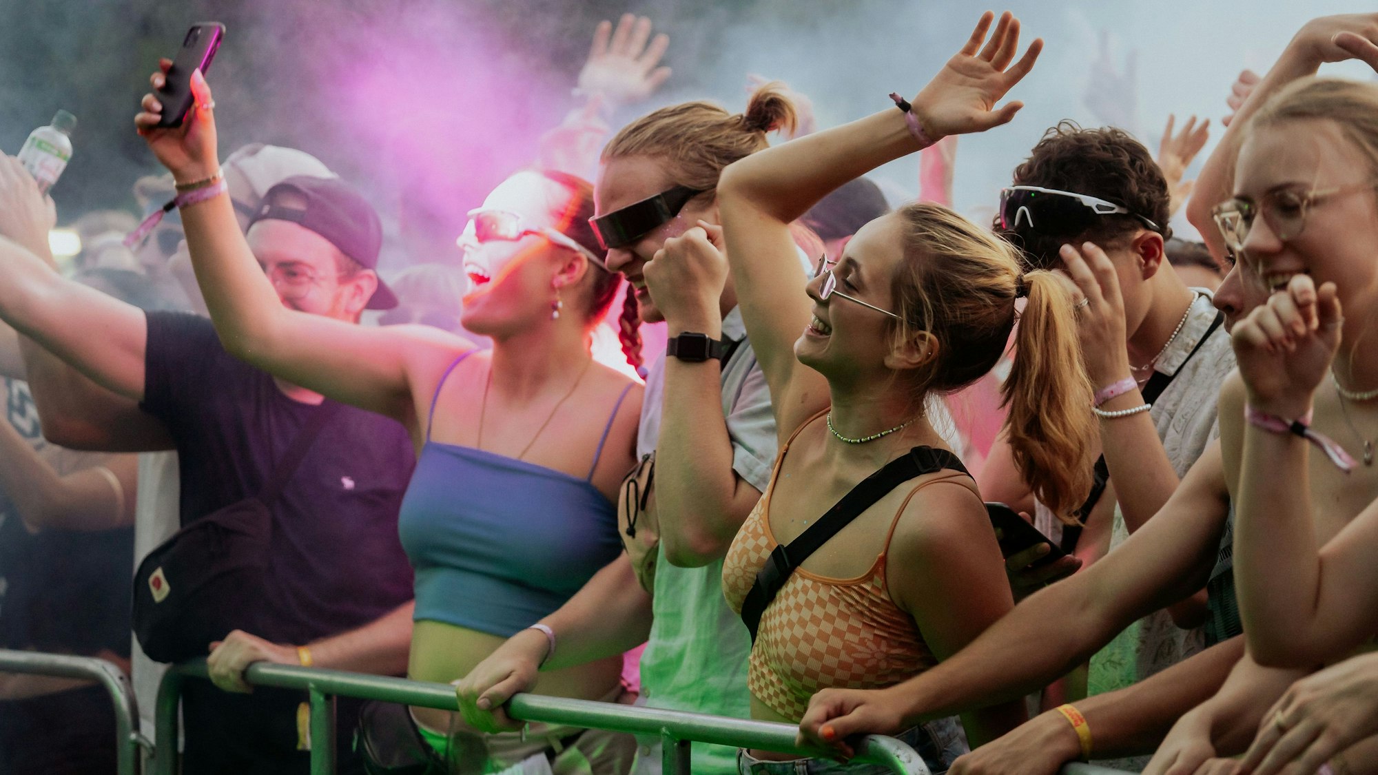 Menschen stehen an einer Absperrung vor einer Bühne, werfen die Hände in die Luft und feiern zur Musik vom Open-Air-Festival.