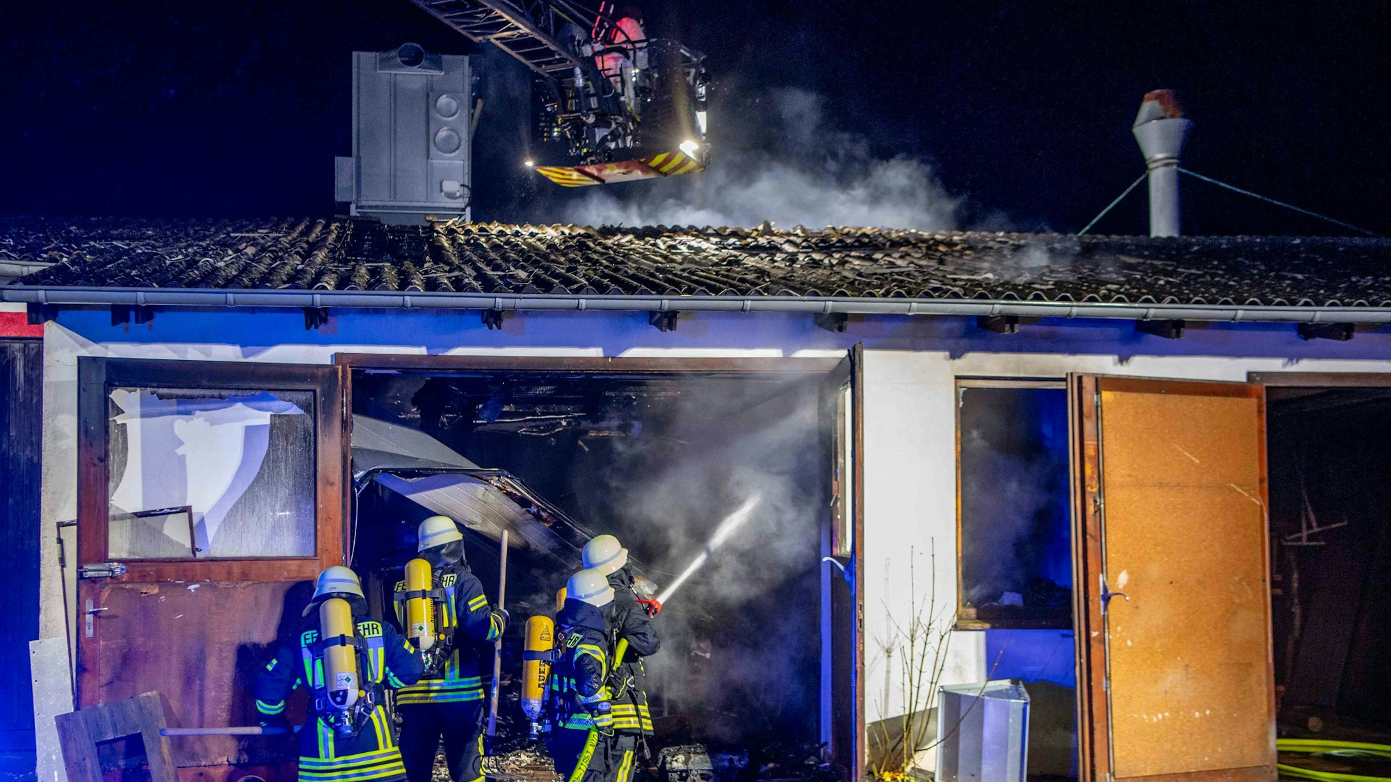 Das Bild zeigt mehrere Feuerwehrleute, wie sie den Brand in der Garage bekämpfen.