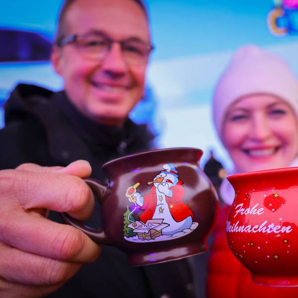 Ein Paar hält zwei Tassen mit heißem Glühwein kurz nach der Eröffnung eines Weihnachtsmarktes in den Händen und stößt an.