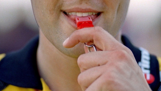 Ein Schiedsrichter nimmt die Pfeife zum Pfiff in den Mund.