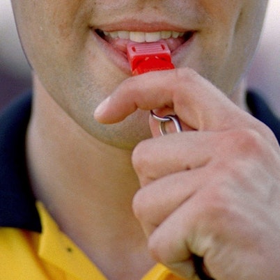 Ein Schiedsrichter nimmt die Pfeife zum Pfiff in den Mund.