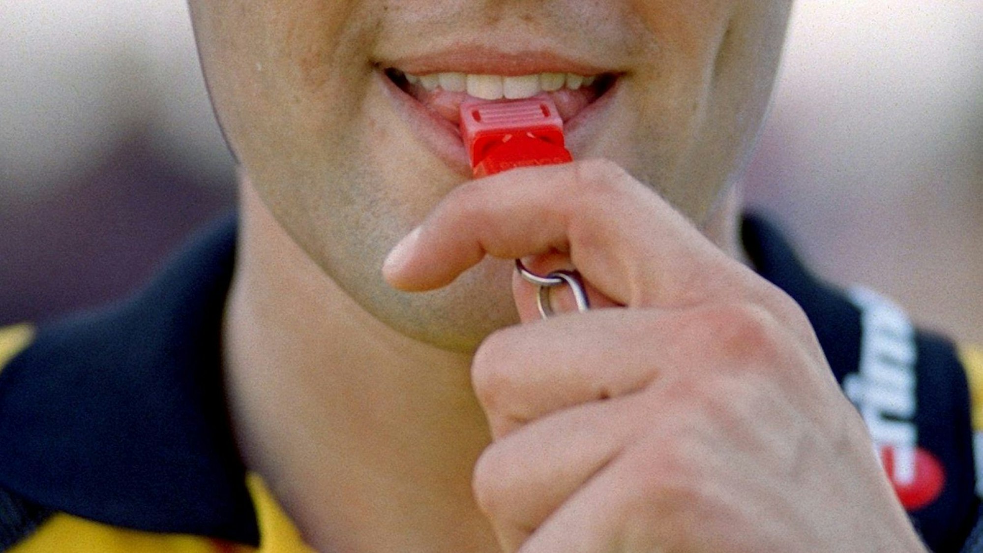 Ein Schiedsrichter nimmt die Pfeife zum Pfiff in den Mund.