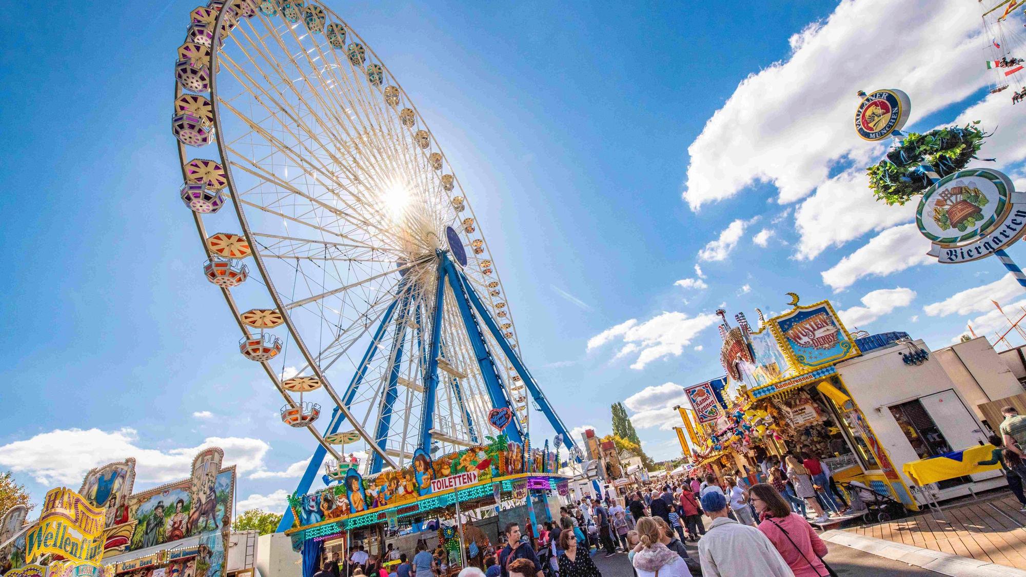 Blick auf Pützchens Markt, auf Buden und das Riesenrad bei blauem Himmel und strahlendem Sonnenschein.
