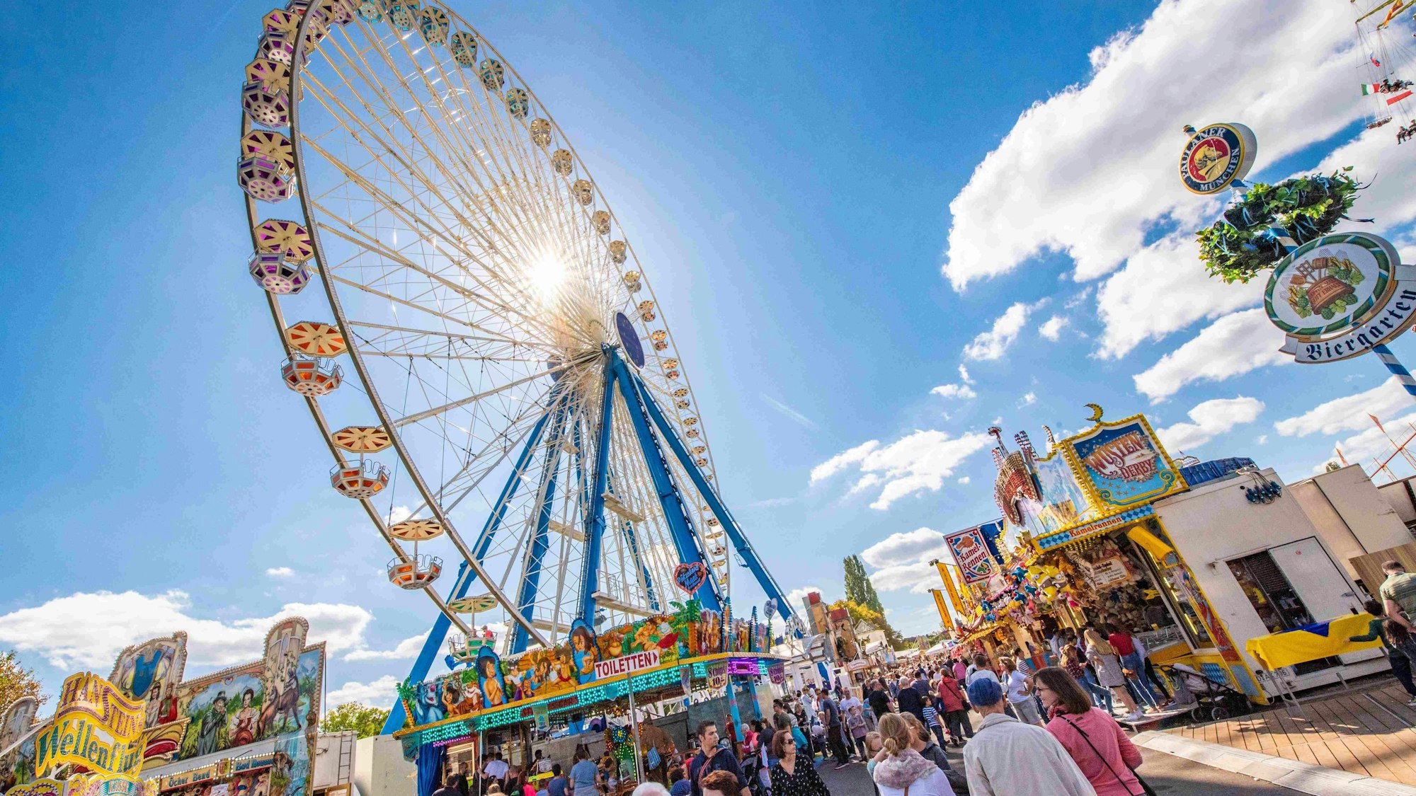 Blick auf Pützchens Markt, auf Buden und das Riesenrad bei blauem Himmel und strahlendem Sonnenschein.