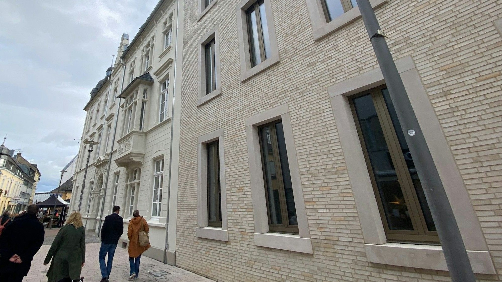 Zu sehen sind das frischsanierte Rathaus und der neue verklinkerte Anbau, an dem einige Passanten vorbeigehen.