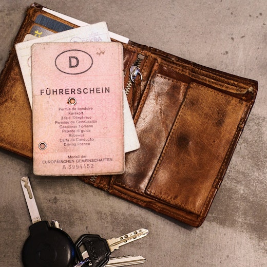 Ein „rosa Führerschein“, ein Autoschlüssel, eine Geldbörse und ein Fahrzeugschein liegen auf dem Tisch