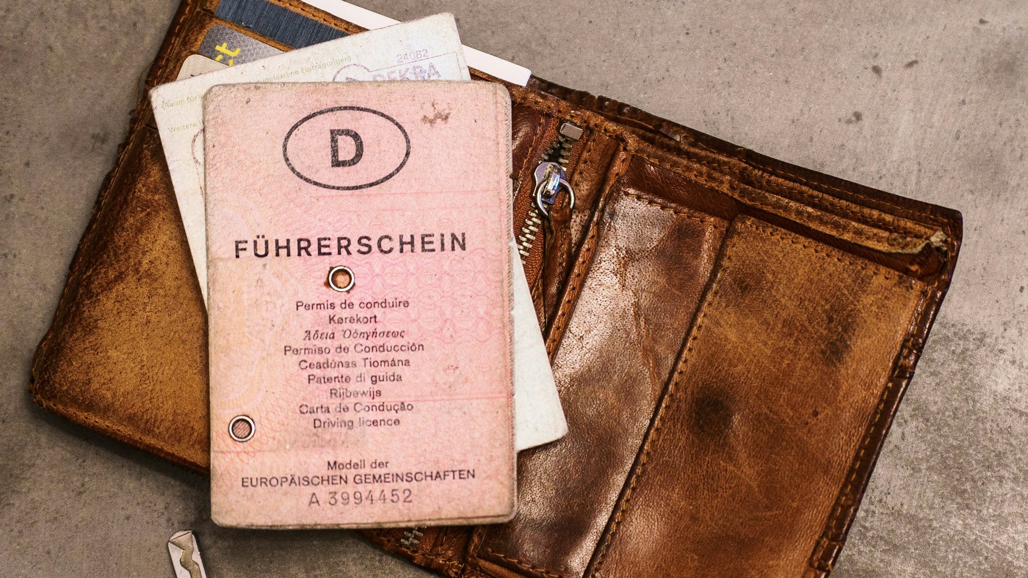 Ein „rosa Führerschein“, ein Autoschlüssel, eine Geldbörse und ein Fahrzeugschein liegen auf dem Tisch