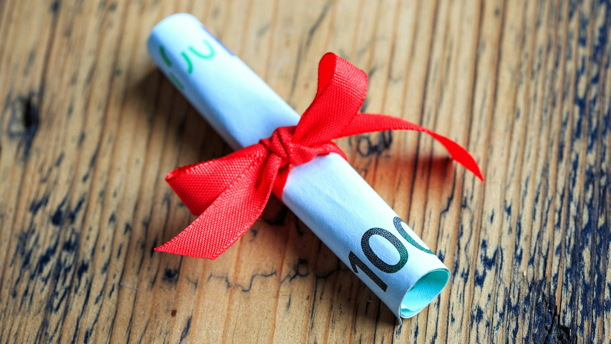 100 Euro Schein eingerollt und mit Schleife als Geschenk verpackt