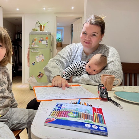 Eine Mutter sitzt mit ihren beiden Kindern an einem Tisch. Vor ihnen liegen Malstifte und Papier.