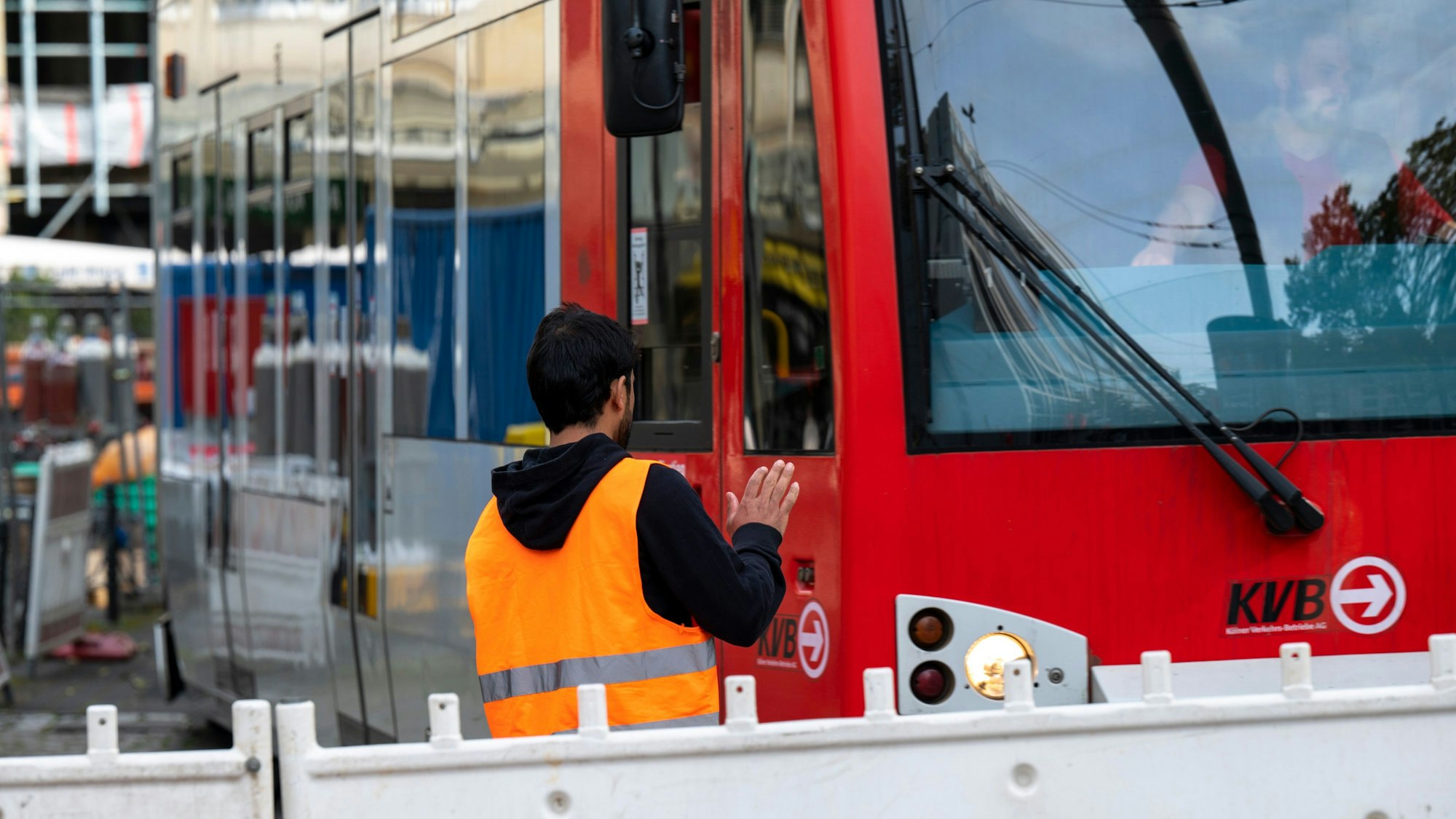 Ein Arbeiter in Warnweste steht vor einer Absperrbake, an der eine Straßenbahn vorüber fährt.