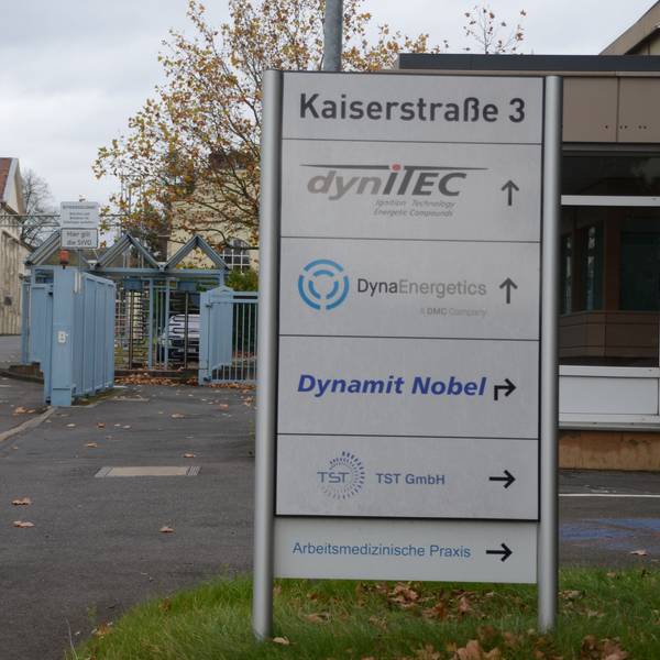 Die Einfahrt zu einem Industriepark. Auf einem Schild stehen mehrere Firmennamen.