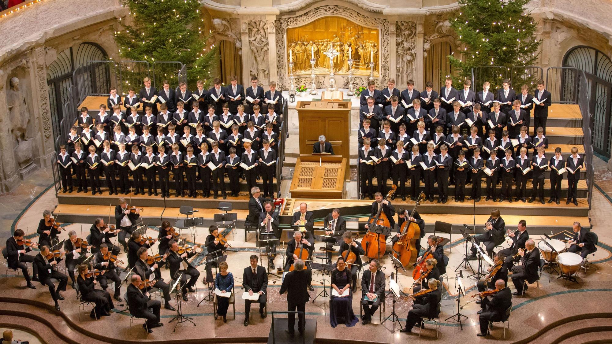 Aus der Vogelperspektive sieht man das das Orchester und den Chor in der Dresdner Kreuzkirche. Hinter dem Chor sind zwei geschmückte Tannenbäume.
