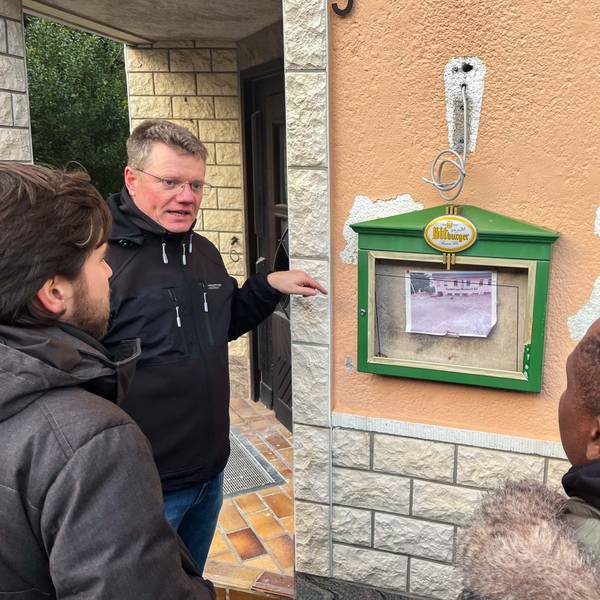 Das Bild zeigt Karl Kreuzberg vor der Gaststätte in Schweinheim. Menschen aus Ghana hören ihm zu.